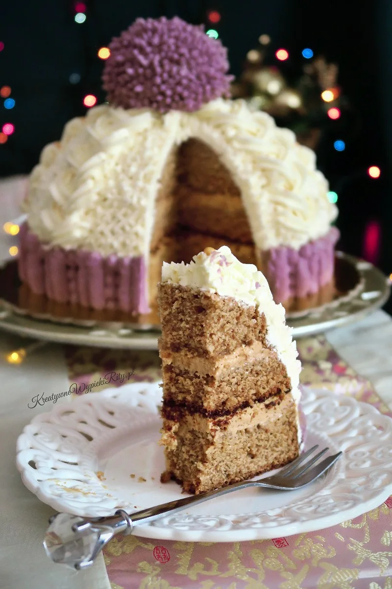 Tort czapka w przekroju na talerzyku, pokazujący warstwy wilgotnego ciasta piernikowego i kremu kajmakowego z orzechami.
