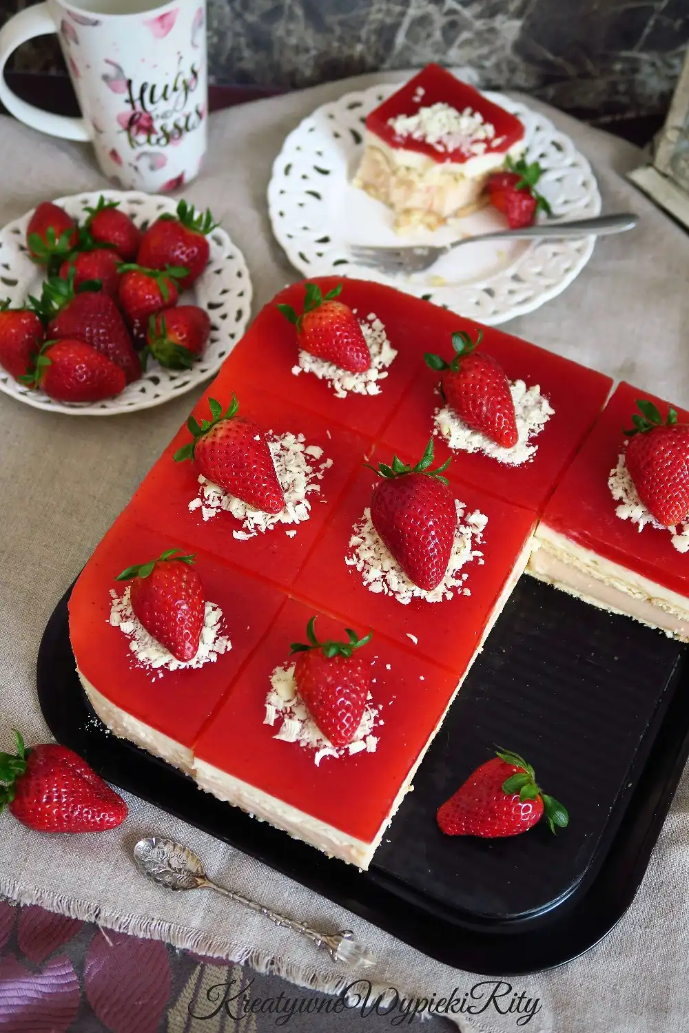 Cały budyniowiec truskawkowy bez pieczenia udekorowany wiórkami białej czekolady i świeżymi truskawkami.