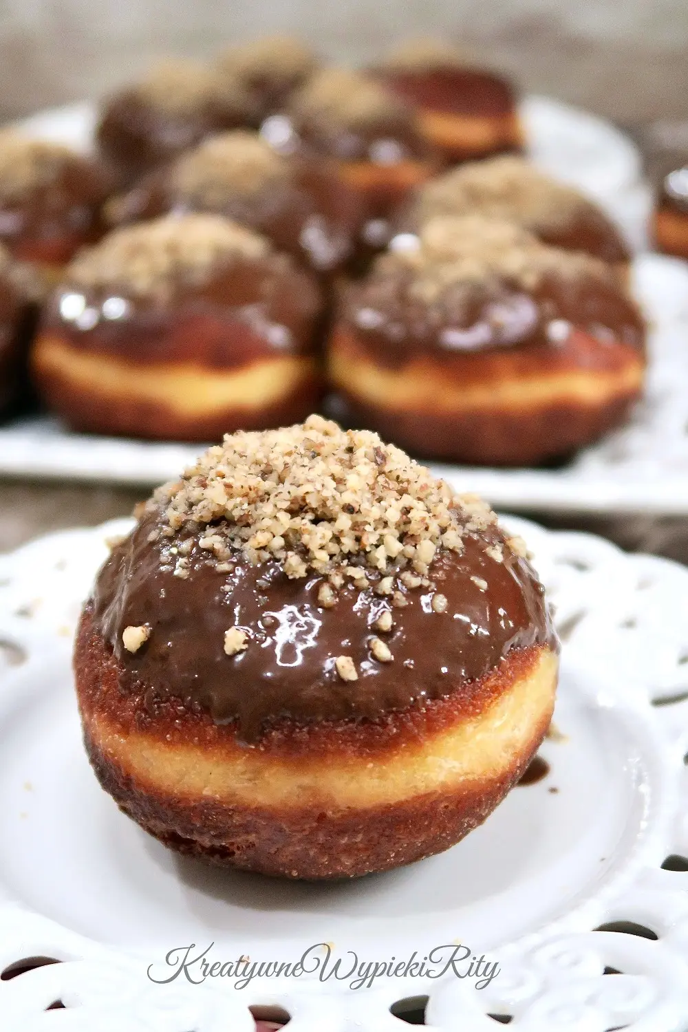 Zbliżenie na pojedynczego pączka na talerzyku – widoczna lśniąca polewa i drobno zmielone orzechy.