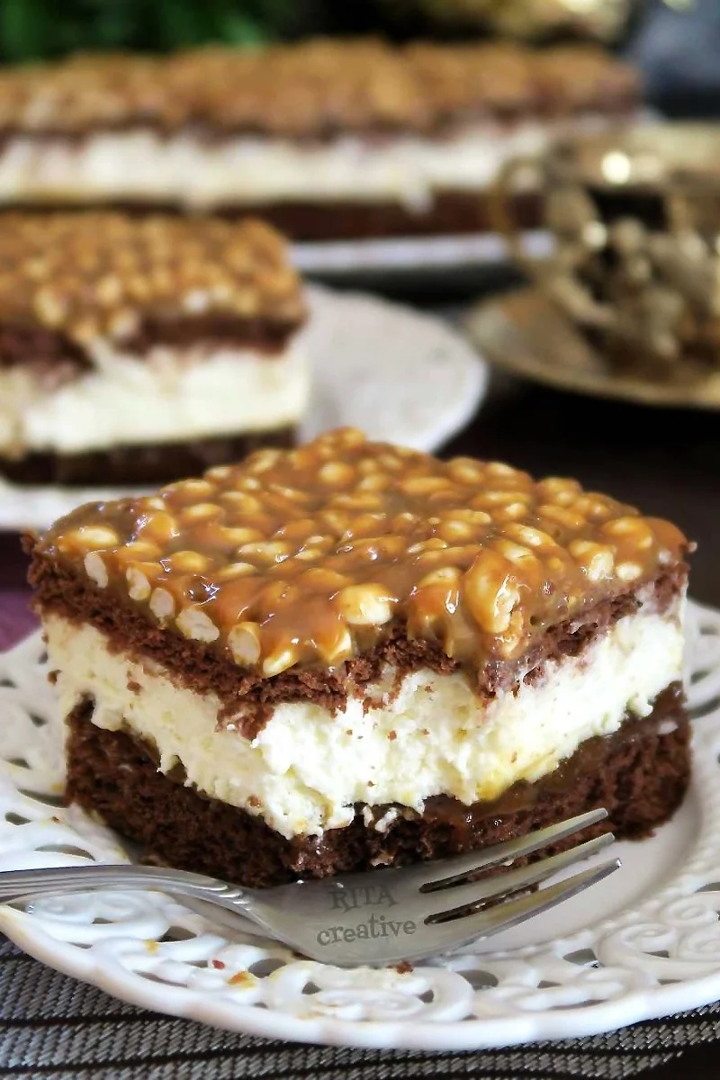 Zbliżenie na wierzch ciasta Szyszkowy Król. Złocista masa kajmakowa wymieszana z białym ryżem preparowanym rozłożona na ciemnych herbatnikach.