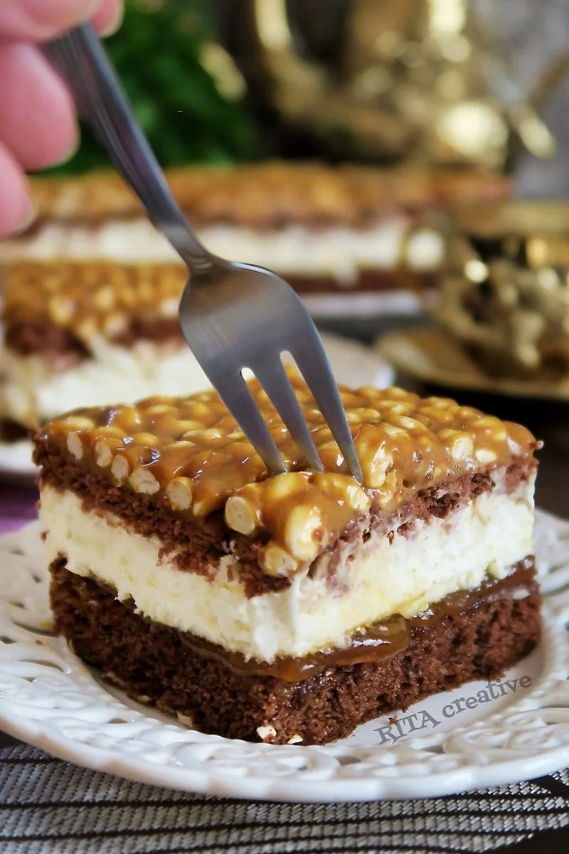 Ciasto Szyszkowy Król. Na talerzu widoczny kawałek ciasta, ciemny kakaowy biszkopt, biały krem śmietankowy oraz wierzch z masy krówkowej i ryżu preparowanego.