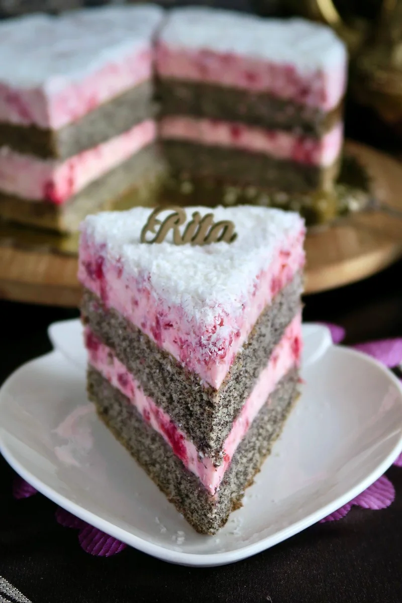 Wysoki kawałek tortu makowego przełożony dwiema warstwami różowego kremu malinowego.