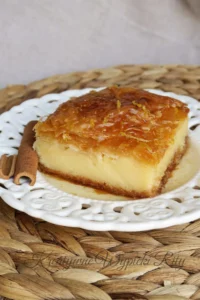 Kawałek greckiego ciasta Galaktoboureko na talerzu, widoczne chrupiące warstwy ciasta filo i gęsty krem z kaszy manny.