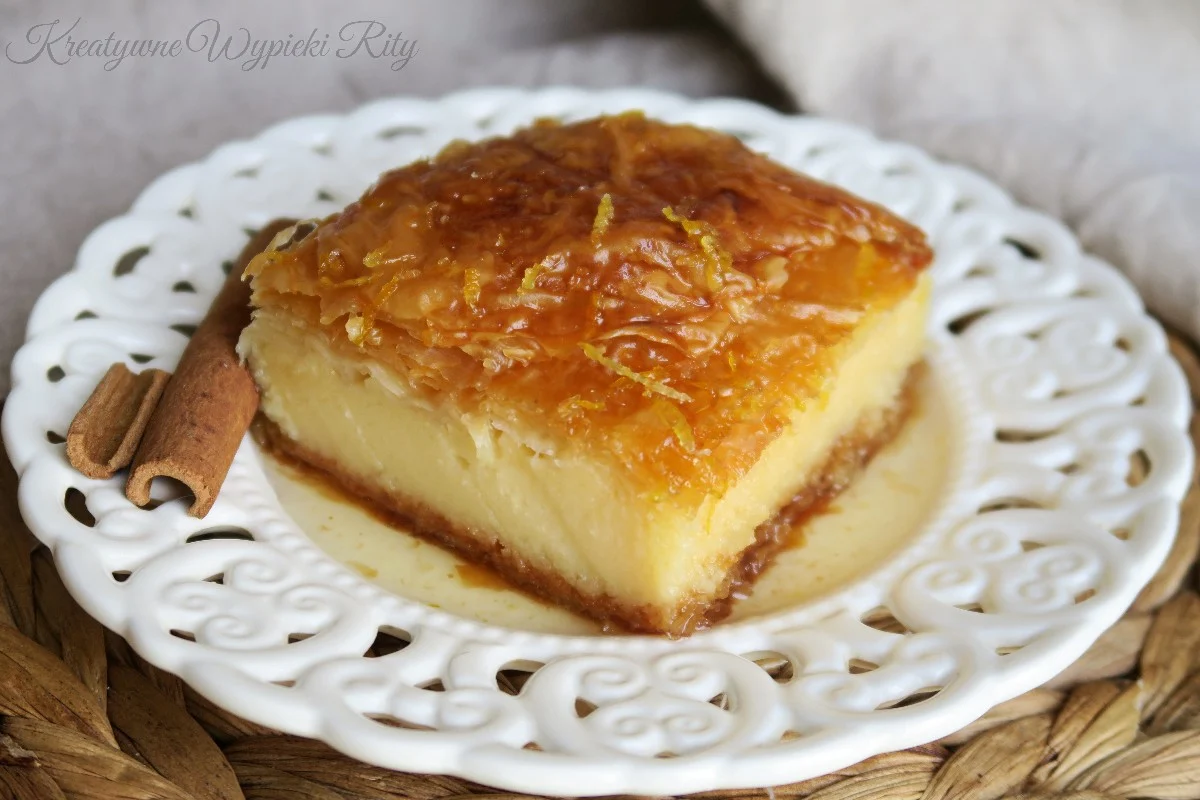  Zbliżenie na przekrój ciasta Galaktoboureko pokazujące grubą warstwę kremu budyniowego między listkami ciasta filo.